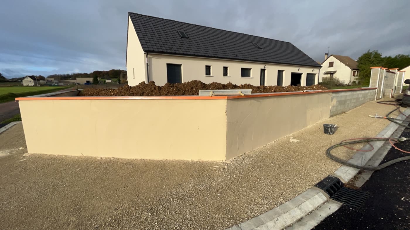 Mur de clôture en cours d'enduit, finition grattée, devant une maison neuve